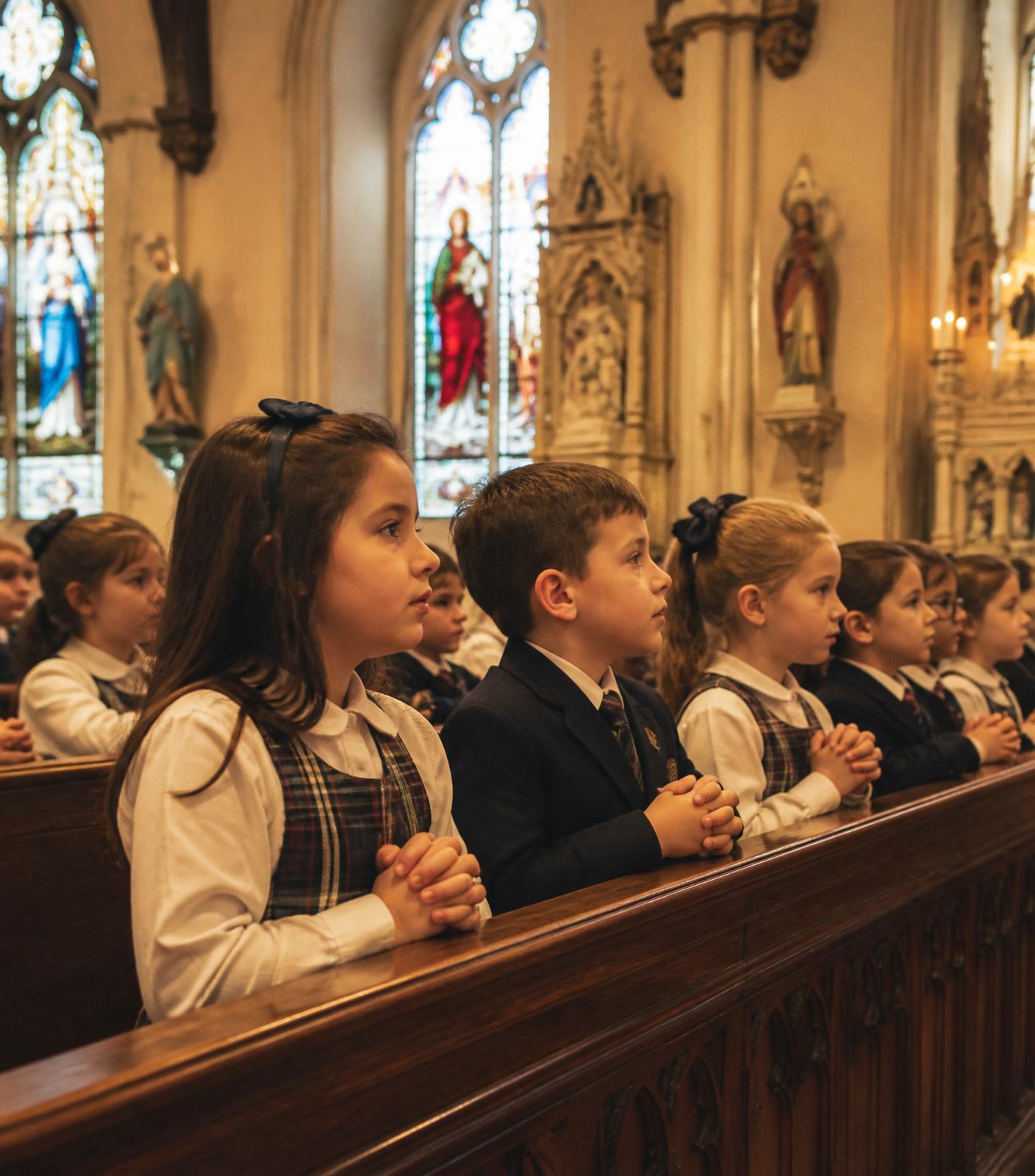 Catholic school children in uniform kneel reverently in the pews of a beautiful traditional church.
